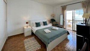 A hotel room with a bed, a nightstand, a chair, a mirror, and a balcony with a view.