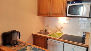 Una cocina compacta con muebles de madera, microondas, cafetera y lavavajillas.