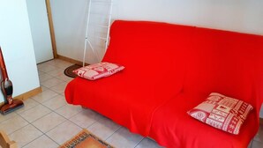 Un sofá rojo con cojines estampados en una habitación con piso de baldosas y pared blanca.
