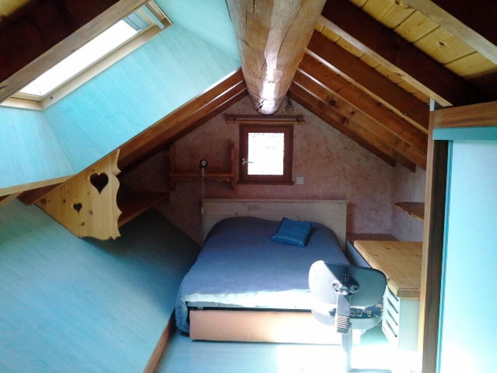 Une petite chambre mansardée avec un plafond en pente, un lit simple, une petite fenêtre et un radiateur.