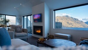 A modern living room with a fireplace, comfortable seating, a television, and a large window with a mountain view. - Villa Awa | Lake Views,BBQ,Fireplace, Free Parking (Queenstown)