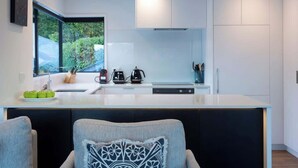 A modern kitchen with a large window, white cabinetry, and a central island with appliances. - Villa Awa | Lake Views,BBQ,Fireplace, Free Parking (Queenstown)