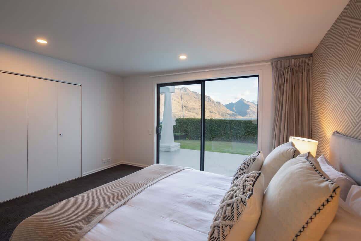 A bedroom with a bed, a large window with a mountain view, a sliding door, and a patterned wall.