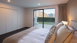 A bedroom with a bed, a large window with a mountain view, a sliding door, and a patterned wall. - Villa Awa | Lake Views,BBQ,Fireplace, Free Parking (Queenstown)