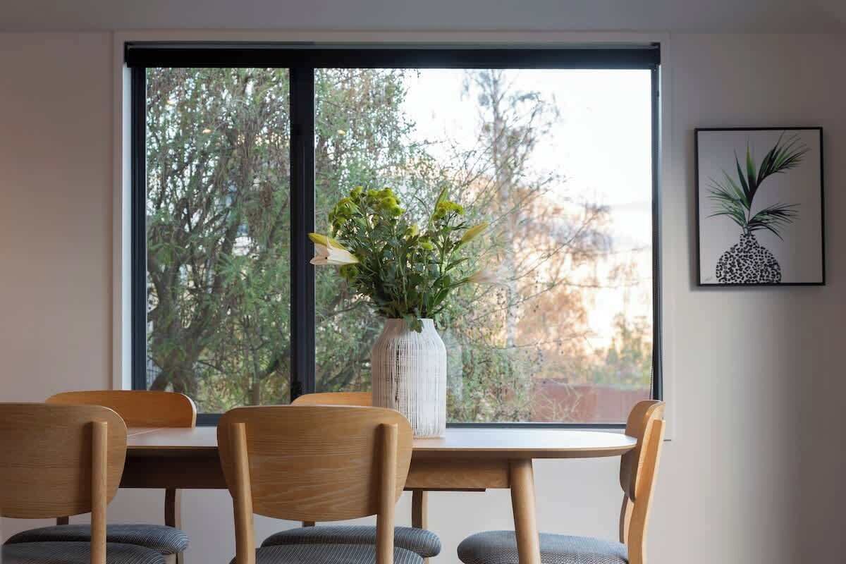 A dining area with a table and chairs, a vase with flowers, and a framed picture on the wall.