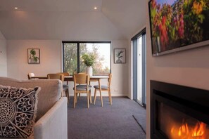 Un salon moderne doté d’une cheminée, d’un coin repas avec une table et des chaises, et de grandes fenêtres offrant une vue sur l’extérieur.