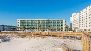 A beachfront hotel with multiple floors, a sandy beach in the foreground, and palm trees. - Royal Gulf Beach & Racquet 5302 - Beautiful Studio Gulf Front Unit! (Gulf Shores)
