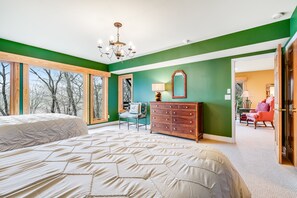 A bedroom with two beds, a dresser, a chair, and a view of the outdoors.