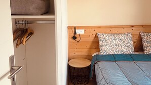 Ein Schlafzimmer mit einem Bett, einem kleinen runden Tisch, einem Holzkopfende, einem Regal mit einer Decke und einem Kleiderhaken mit Holzgegenständen.