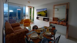 Una sala moderna con un sofá, una mesa de comedor para cuatro personas, un televisor y un espejo grande.