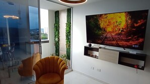 Un salón moderno con un televisor de pantalla plana grande, una mesa de centro de vidrio y un sillón naranja cómodo.