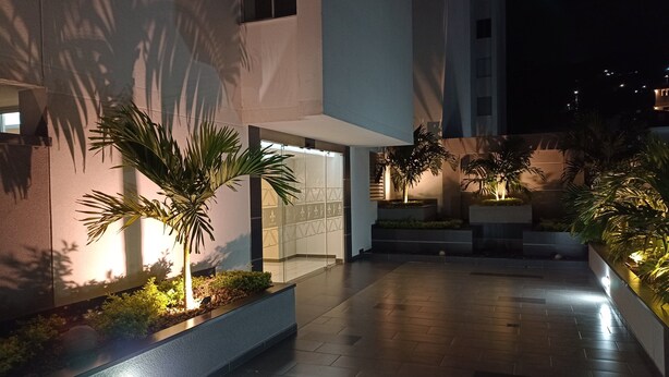 Exterior moderno de un edificio por la noche, con entrada iluminada y jardines aledaños.