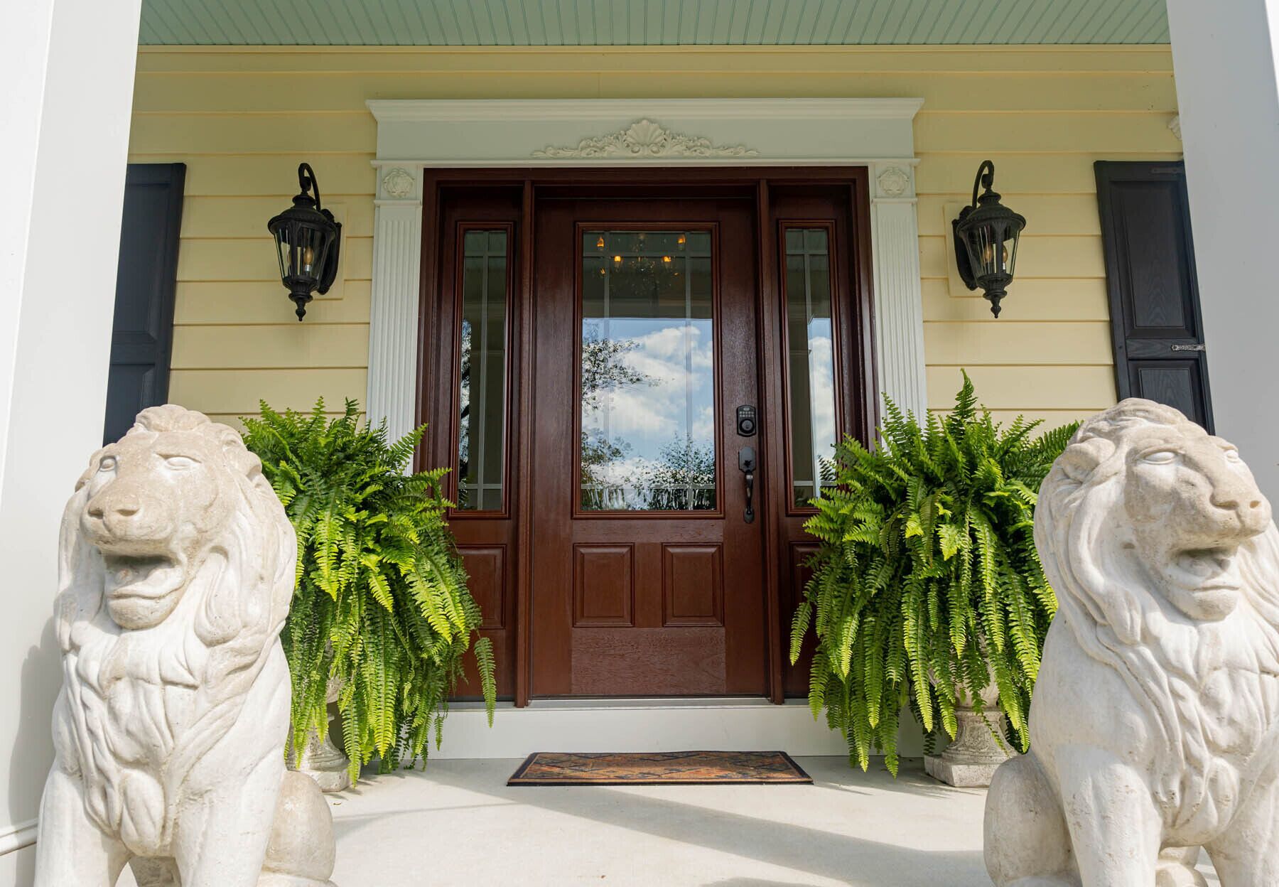 A stately entrance with a wooden double door, two stone lion statues, and a green door mat.