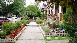 Una calle residencial con coches aparcados, aceras y casas con porches y jardines.