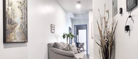 Un couloir avec un canapé gris, un tableau, une plante et un porte-chaussures.