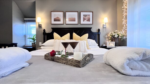 Una habitación de hotel con una cama, dos lámparas de noche, una mesita de noche con un florero y tres cuadros en la pared.