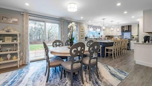 Een moderne keuken met een centraal eiland, een eetgedeelte met een ronde tafel en stoelen, en uitzicht op de omgeving.