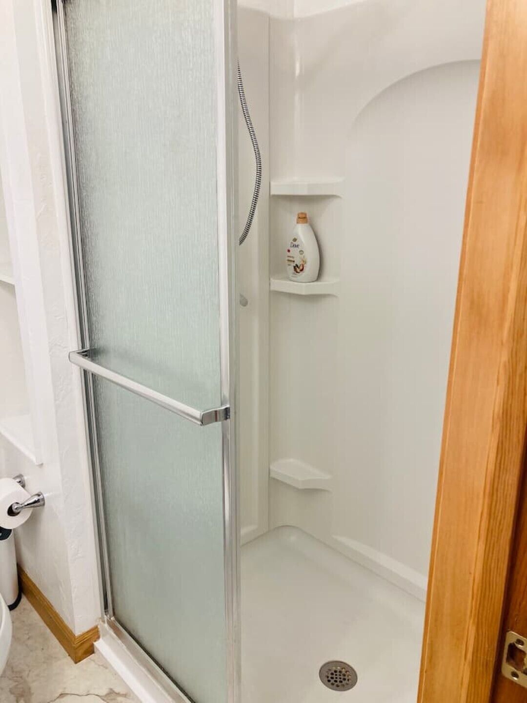 A glass-enclosed shower stall with a metal handle and a shelf with toiletries.