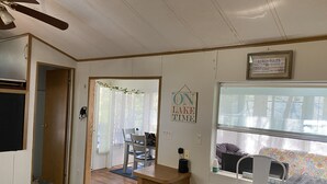 Compact camper interieur met eethoek, een kleine keuken en raam met zonwering.
