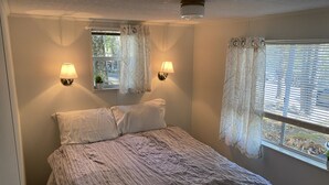 Een slaapkamer met een bed, twee wandlampen en een raam met gordijnen.
