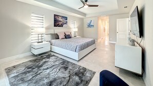 A modern bedroom with a bed, bedside tables, a ceiling fan, and artwork on the walls. -  New Exceptional  Villa Hidden Pearl - Has It All! (Cape Coral)