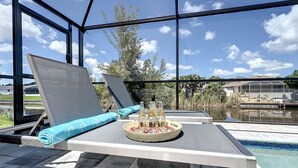 A poolside lounge area with a table set for two, featuring a bottle of beer, a glass, and a plate of snacks. -  New Exceptional  Villa Hidden Pearl - Has It All! (Cape Coral)