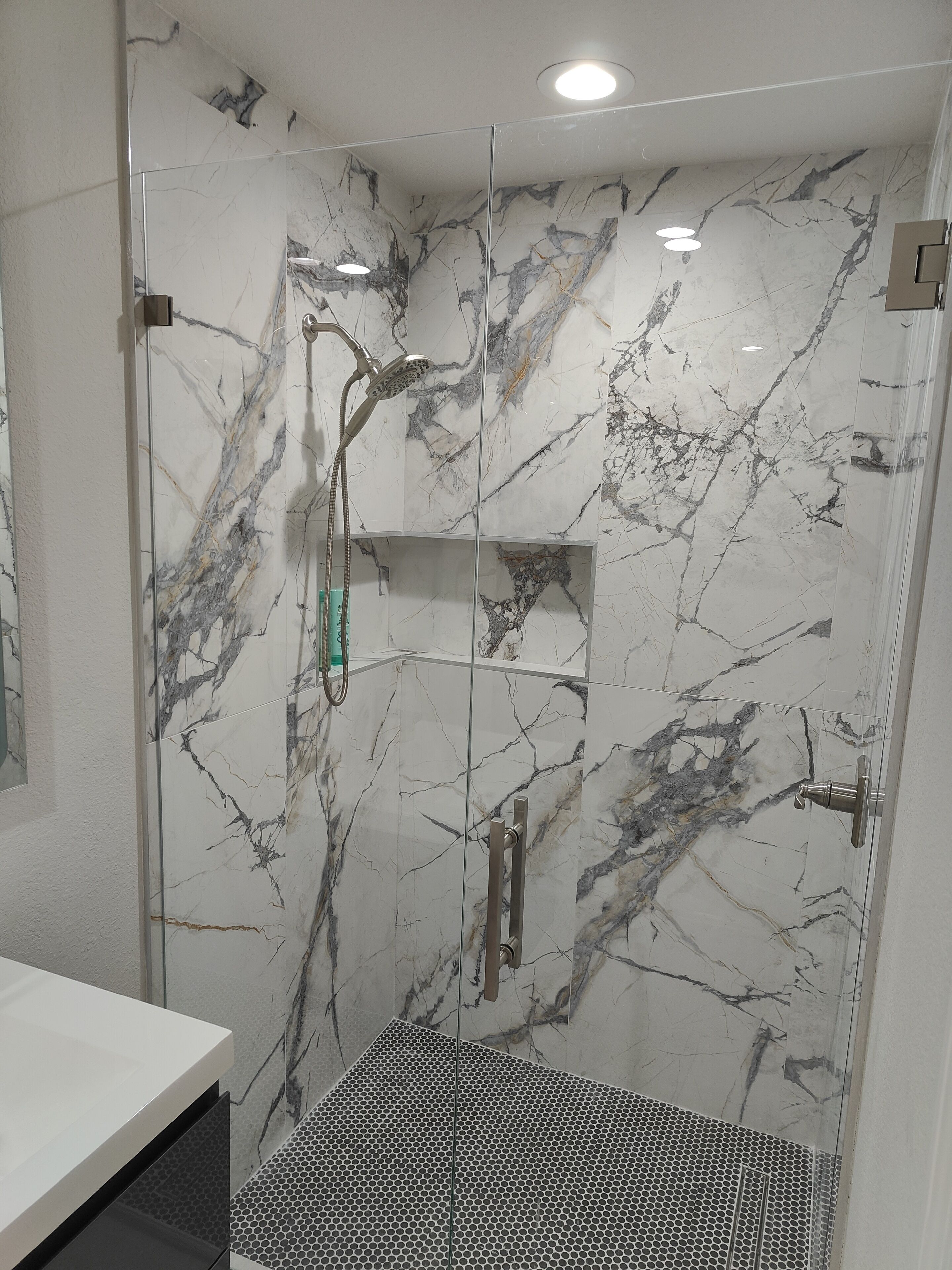 A modern bathroom with a glass-enclosed shower, marble walls, and a white sink.