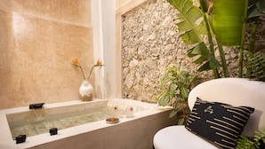 Une salle de bain avec une baignoire, un petit lavabo et une grande plante.