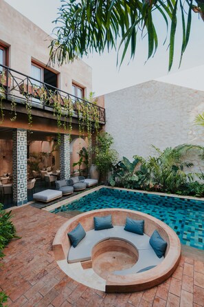 A poolside area with a circular seating arrangement, a covered patio with outdoor furniture, and a stone wall. - CIGNO Ermita Hotel Boutique (Mérida)