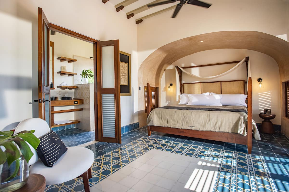A bedroom with a bed, a chair, a mirror, and a bathroom area.