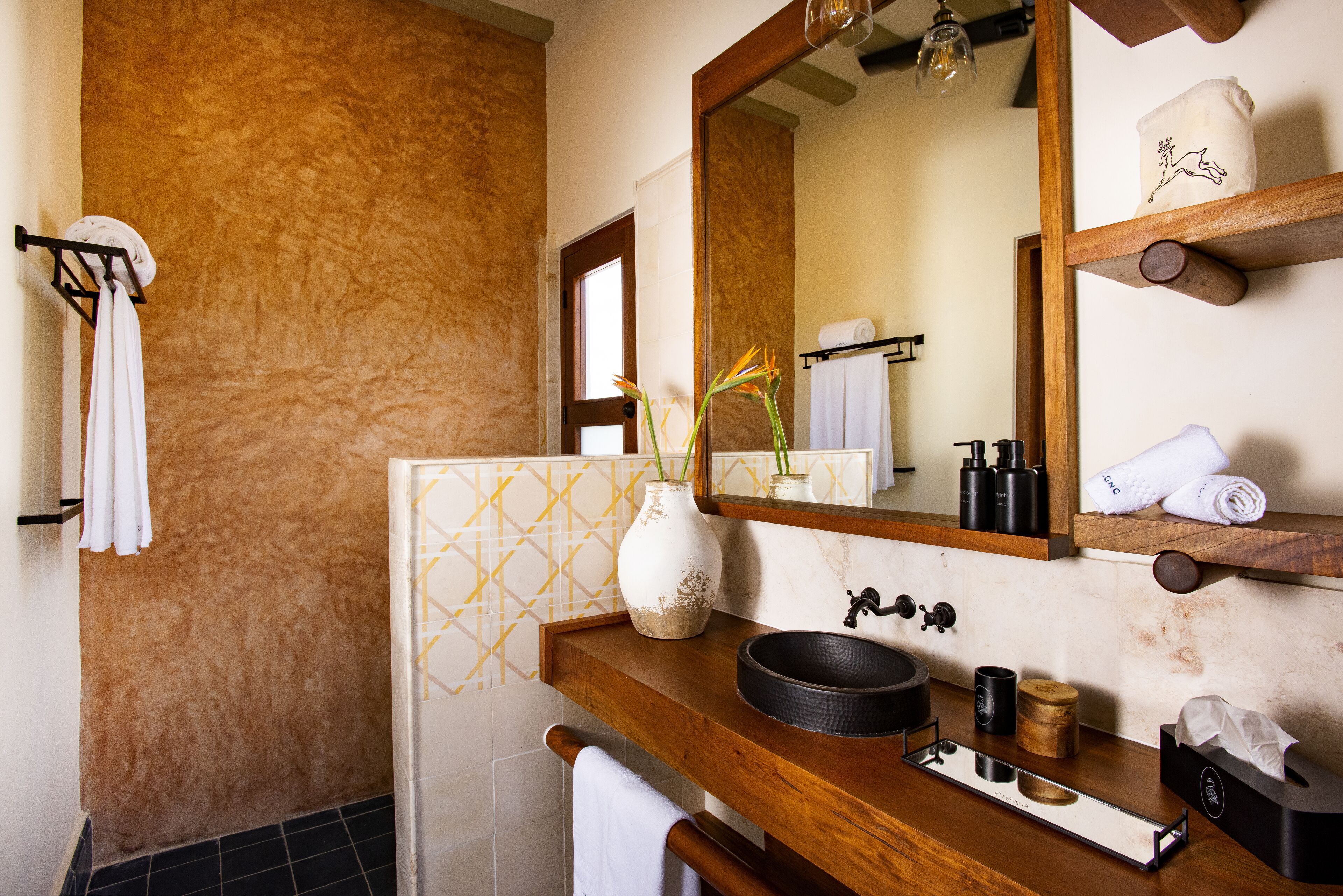 A bathroom with a wooden vanity, a large mirror, a vase with flowers, and towels on the wall.