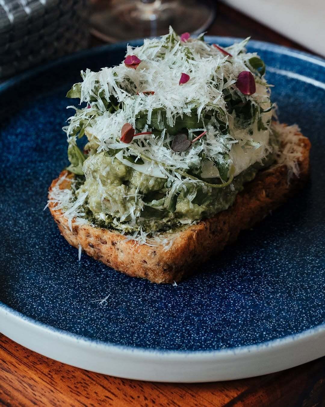 A slice of toast topped with green spread and shredded cheese on a blue plate.