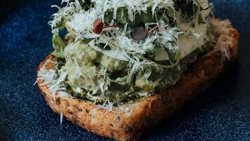 A slice of toast topped with green spread and shredded cheese on a blue plate.