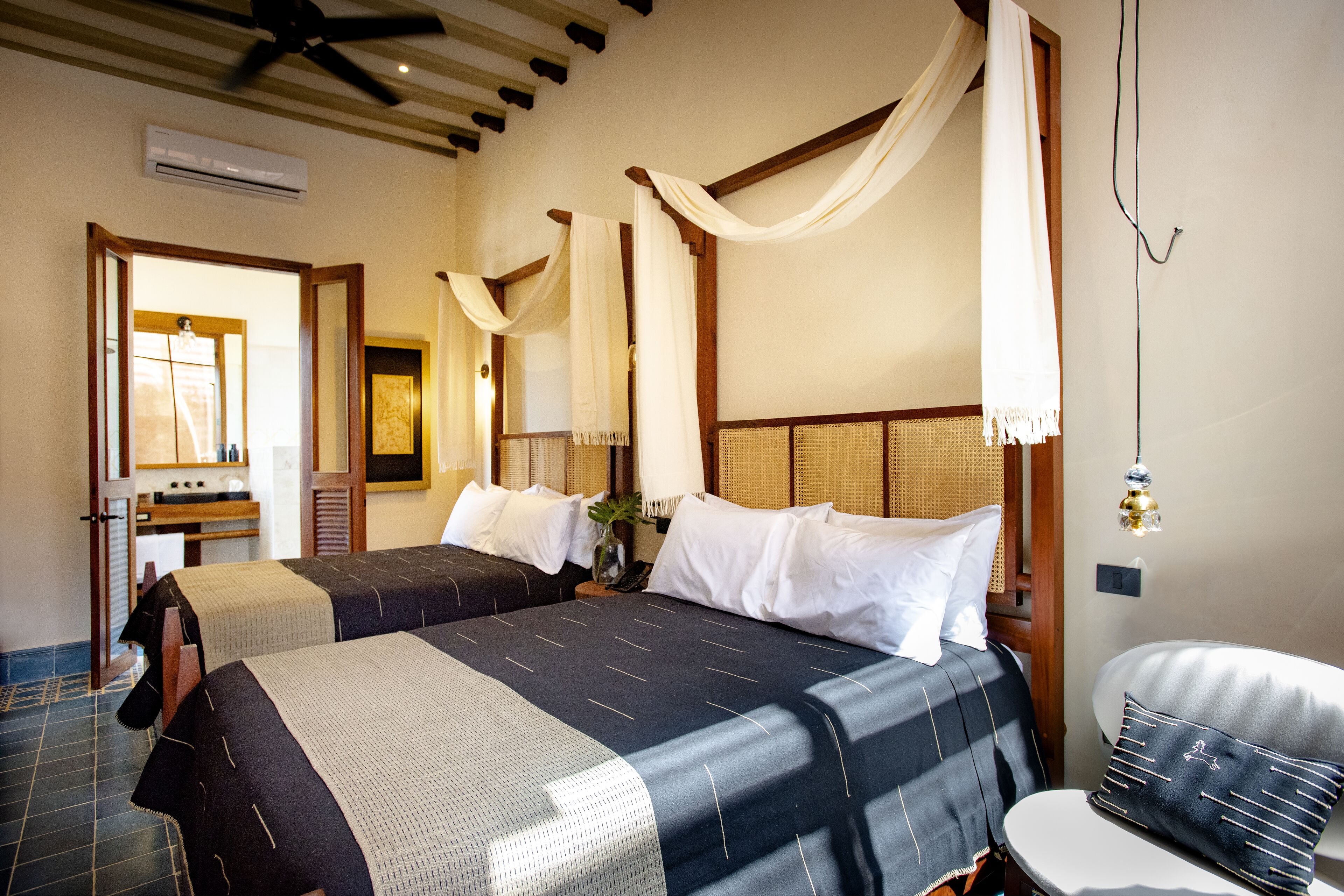 A hotel room with two beds, a desk with a chair, a mirror, and a hanging light fixture.