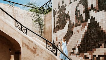 A modern outdoor seating area with a sofa and a table, a staircase with a railing, and a tiled wall with a pixelated design.