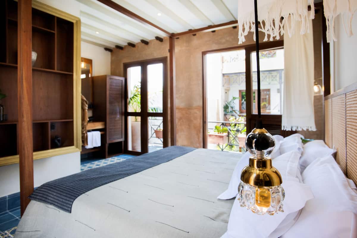 A bedroom with a bed, a bedside table with a bottle, a wooden wardrobe, and a window with a view of the outside.