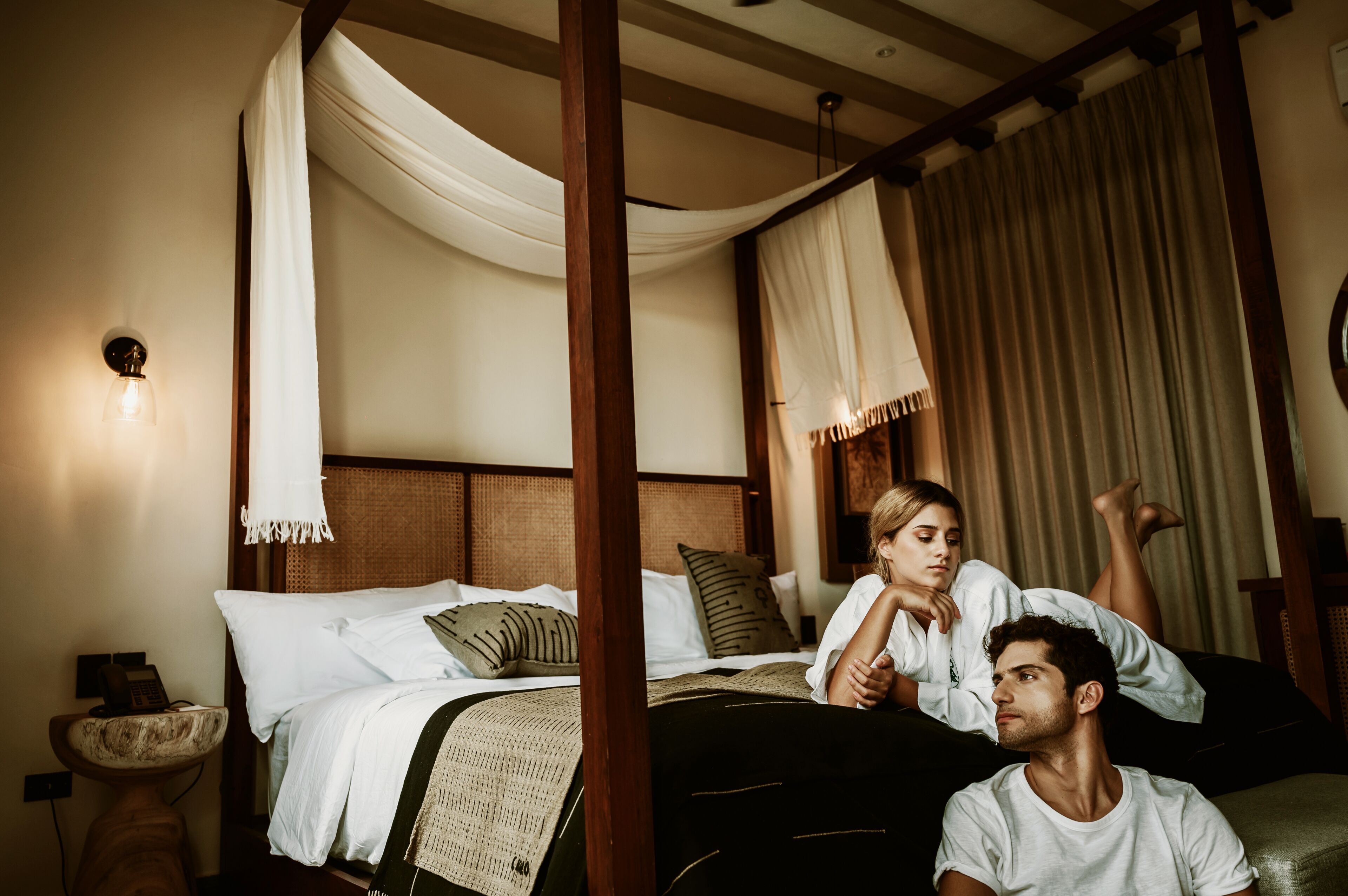 A bedroom with a four-poster bed, a bedside table with a lamp, and a nightstand with a phone.