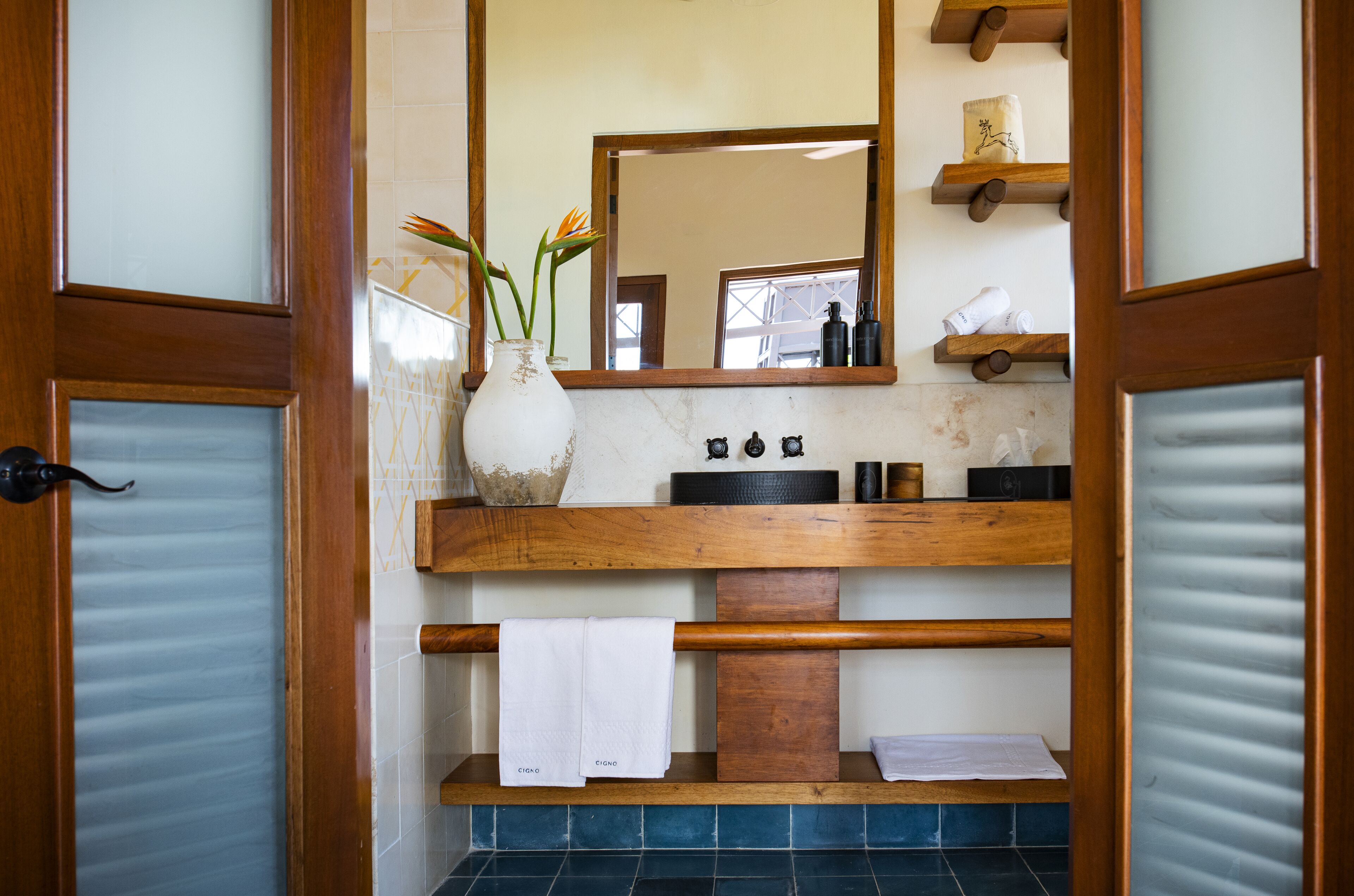 A bathroom with a wooden vanity, a large mirror, and a vase with flowers.