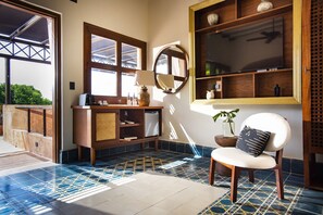 A room with a large TV, a wooden cabinet, a chair, and a tiled floor.