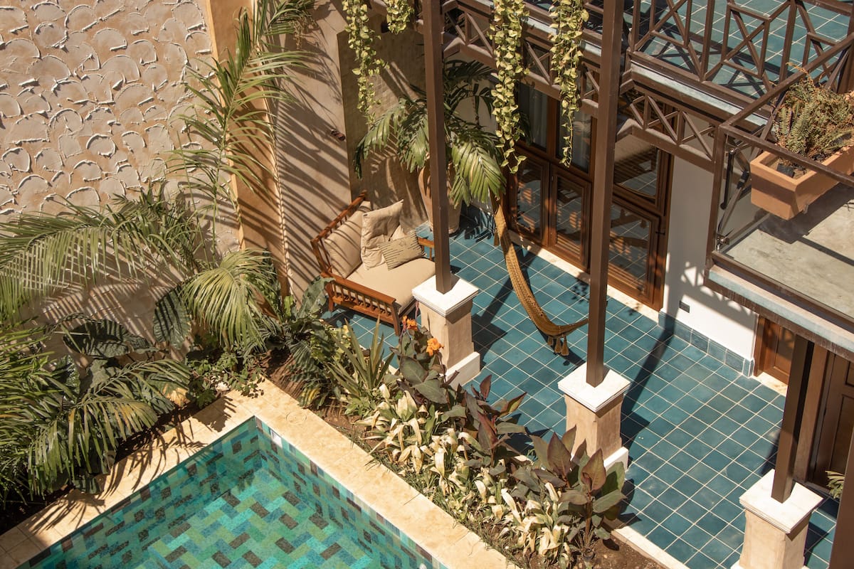 A rooftop pool area with a tiled floor, surrounded by potted plants and a wooden pergola.