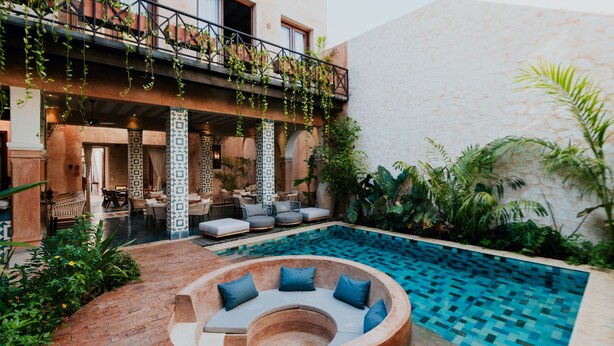Un espace piscine avec des sièges disposés en cercle, un coin repas agrémenté de colonnes décorées et des plantes suspendues.