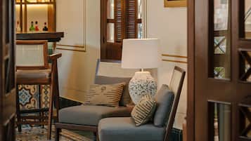 A cozy room with a wooden door, a cushioned chair, a small table, and a shelf with bottles.