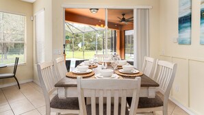 Un coin repas avec une table en bois dressée pour six personnes, entourée de chaises blanches dotées d’assises rembourrées.