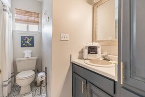 A bathroom with a toilet, sink, and mirror. There is a towel rack with a towel, a picture on the wall, and a small trash bin. - House for 6 - Golf Cart (street legal), pvt beach (Lower Grand Lagoon)