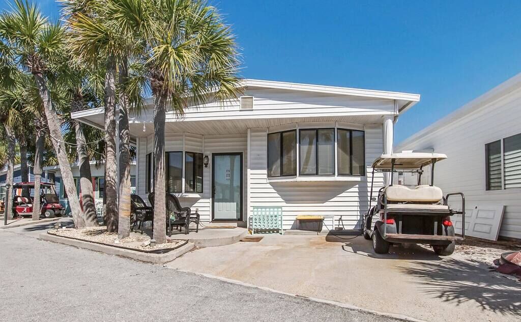 A single-story house with a covered porch, palm trees, and a golf cart parked outside.