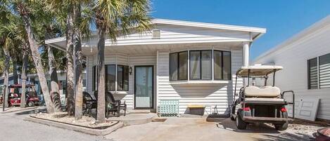 A single-story house with a covered porch, palm trees, and a golf cart parked outside.