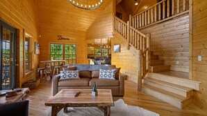 Eine geräumige Holzdiele mit einer gemütlichen Wohnbereitschaft, inklusive einer Couch, einem Couchtisch und einer Treppe zu einer erhöhten Ebene.