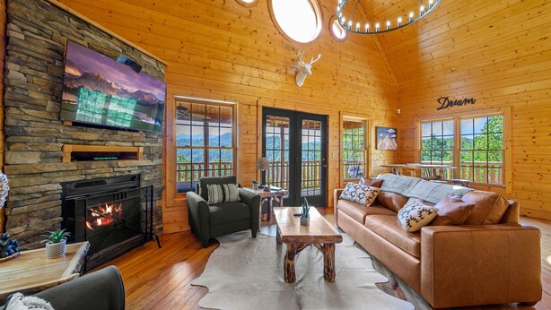 Ein gemütliches Blockhaus-Interieur mit Kamin aus Stein, einem großen Flachbildfernseher, einer Ledersofa und einem Essbereich.