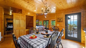 Eine Holzblockhütte mit Essbereich, ausgestattet mit Tischdecke in Karomuster, Stühlen und einer Kristallleuchter.