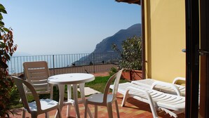A patio with a table and chairs, a sun lounger, and a view of the sea and mountains.